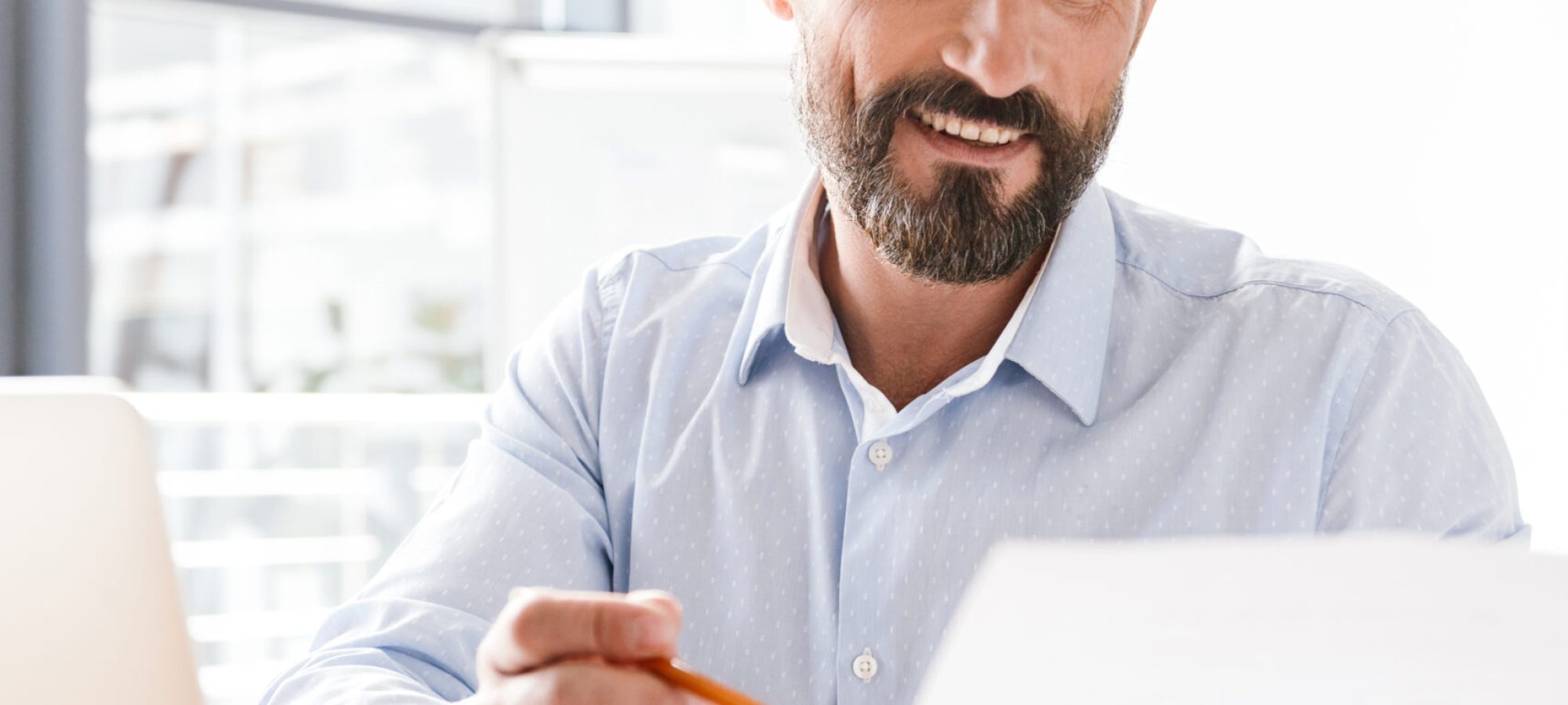 Successful man manager working on laptop computer and documents while sitting at the office with woman co worker on a background